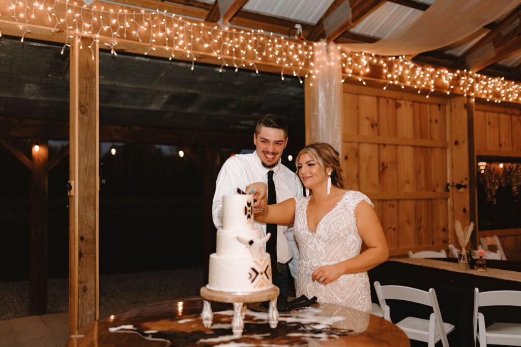 Bride and groom cutting a wedding cake inside a barn decorated with string lights at Montgomery Creek Ranch