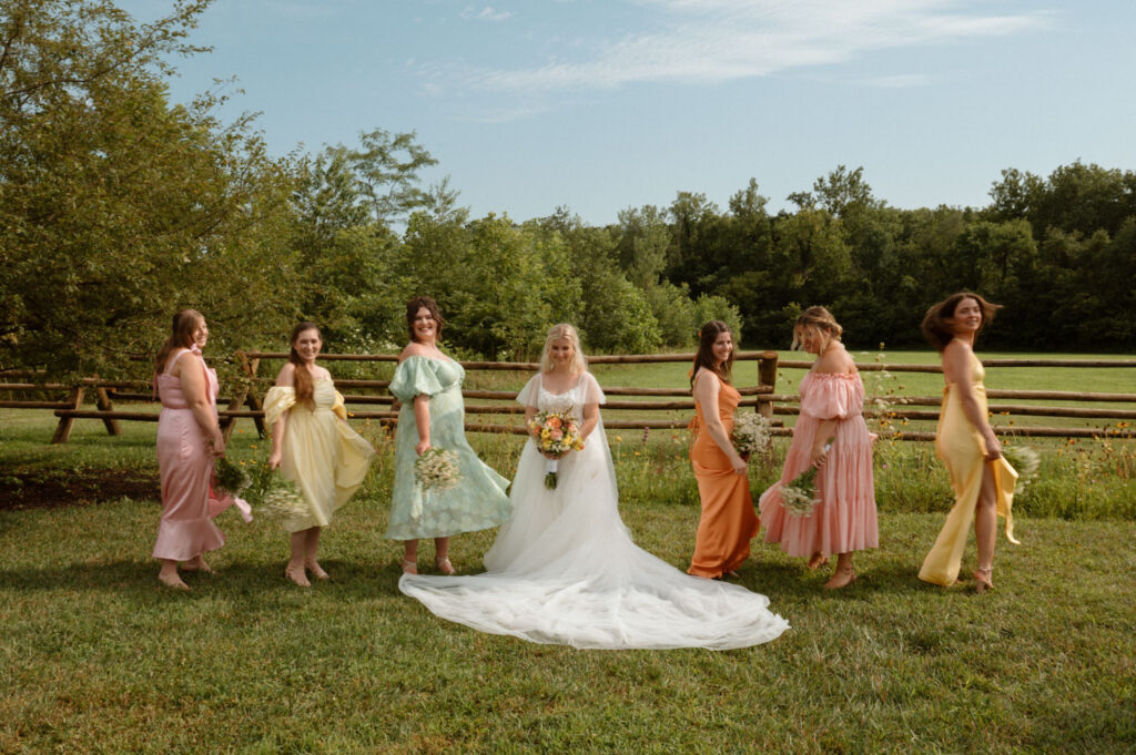 Bride with bridesmaids wearing colorful dresses standing in a grassy field