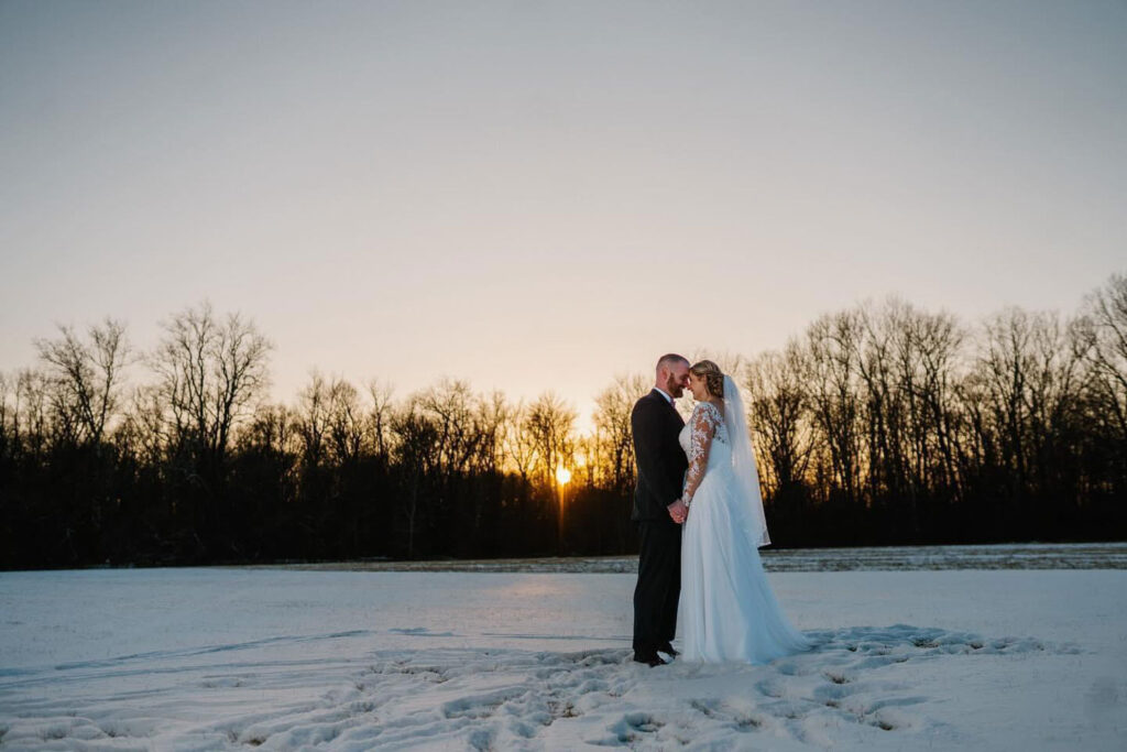 Bride and groom holding hands during sunset in a snowy field