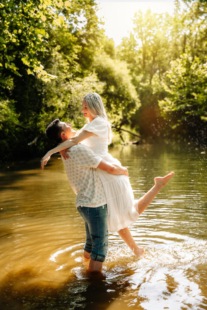 Couple embracing in a sunlit river, surrounded by lush greenery near a wedding location in Indianapolis