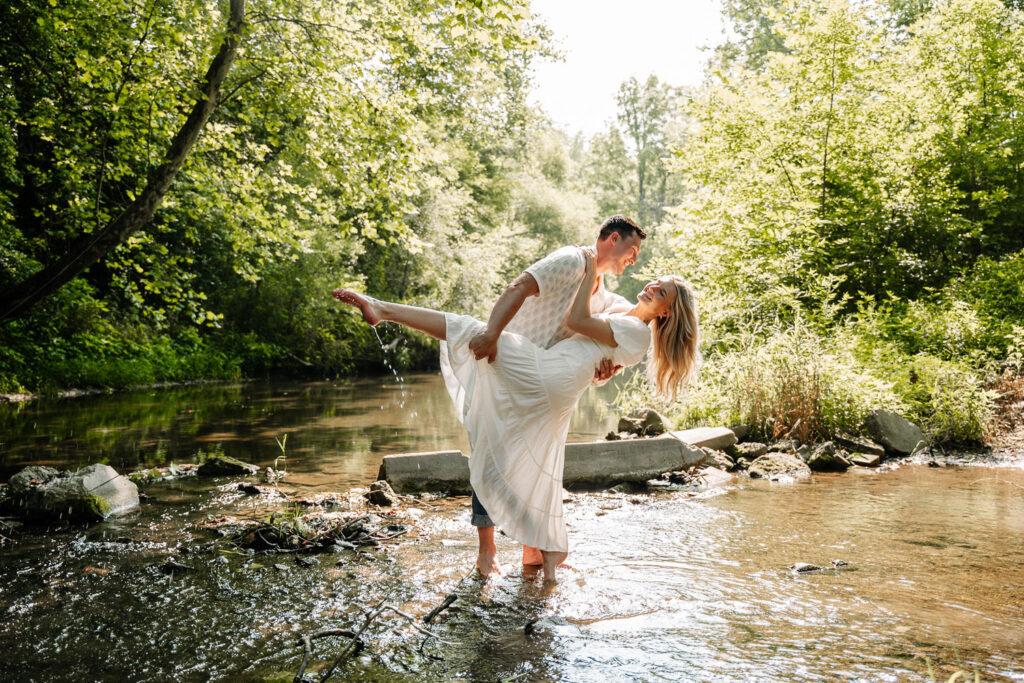 Groom lifting bride in a playful moment in the middle of a sparkling creek