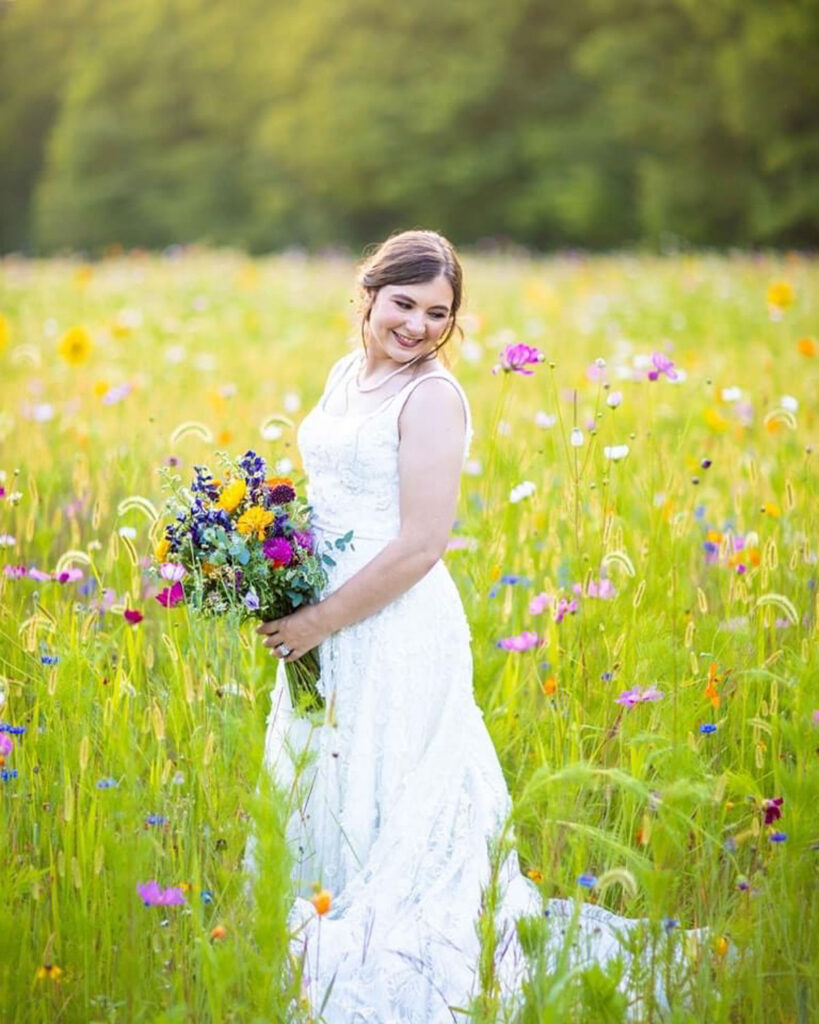 Bride standing in a field of colorful wildflowers holding a vibrant bouquet