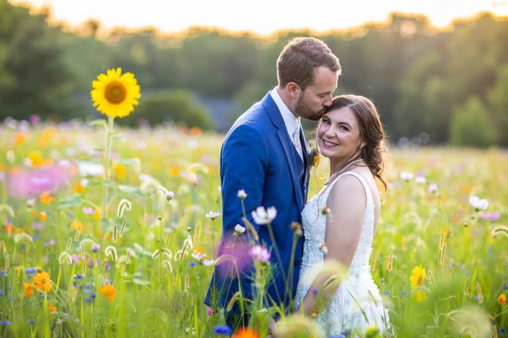 Groom kissing bride’s forehead in a wildflower meadow