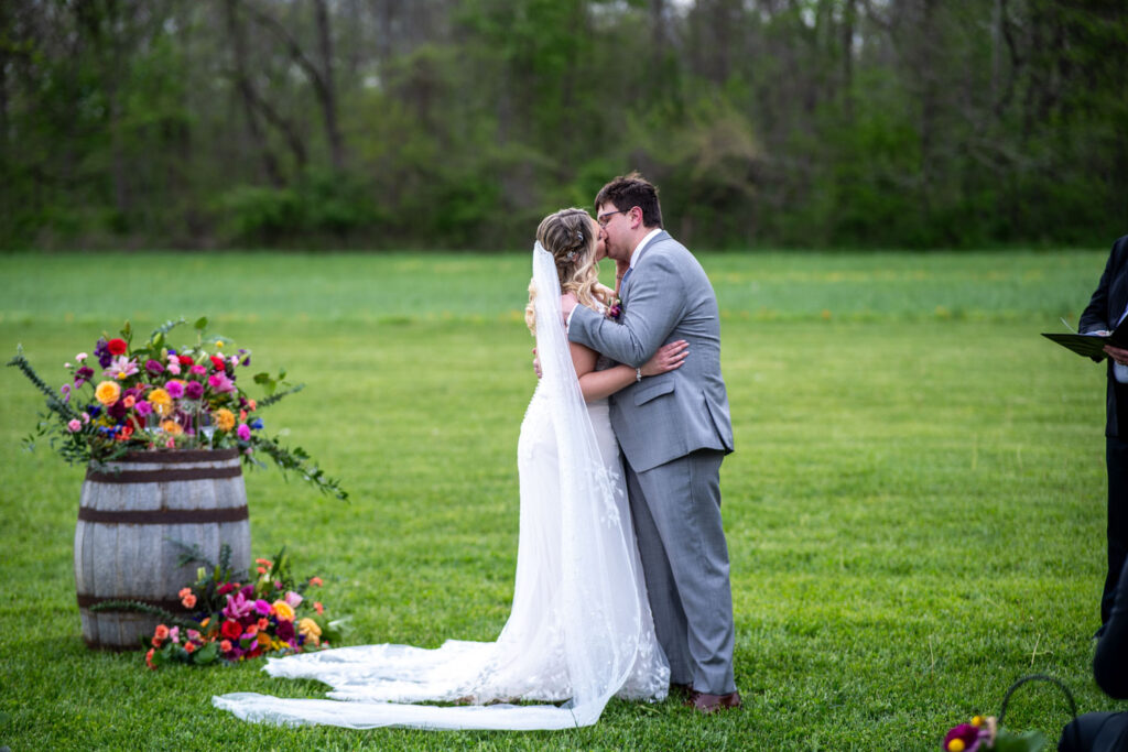 Couple’s first kiss as newlyweds during an outdoor ceremony with vibrant floral arrangements