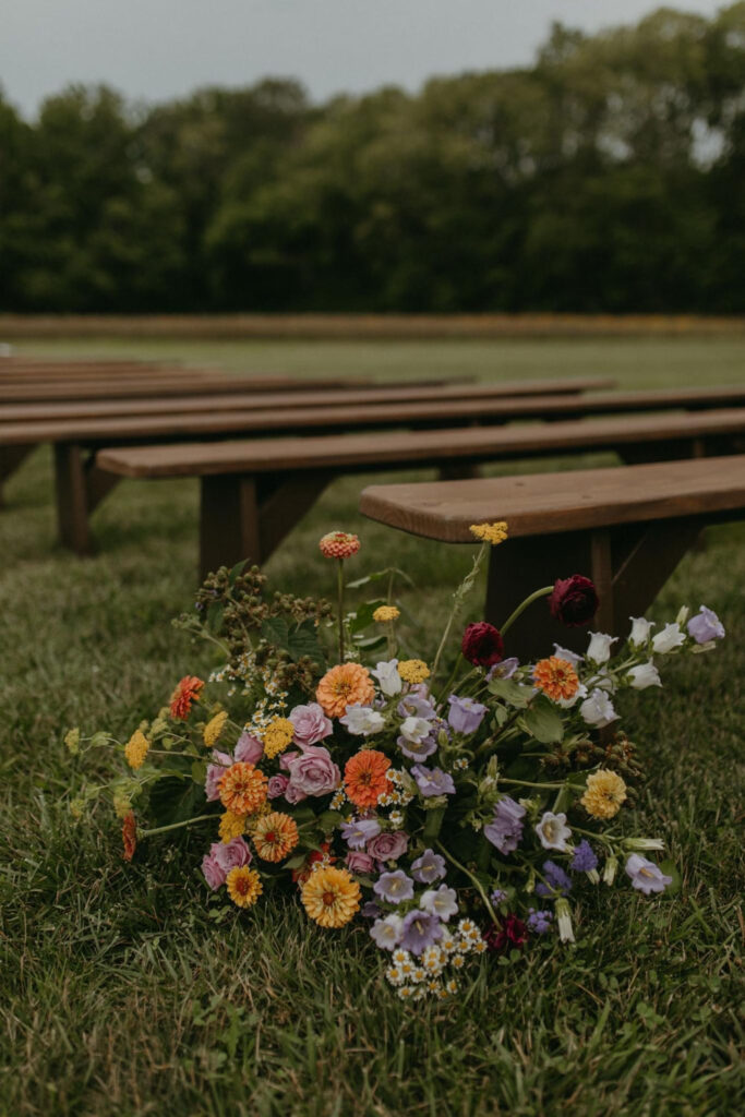 Colorful floral arrangement next to wooden benches at an outdoor wedding