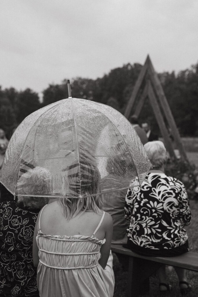 Transparent umbrella shielding guests during a rainy outdoor wedding ceremony