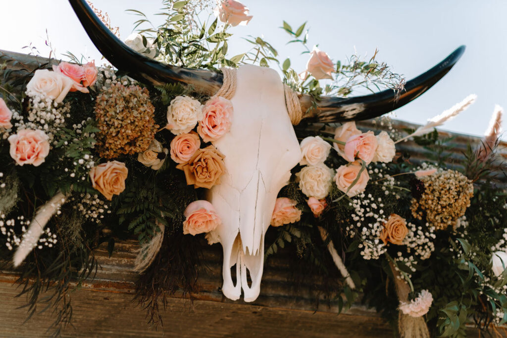 Floral arrangement featuring a cow skull with pastel roses and greenery