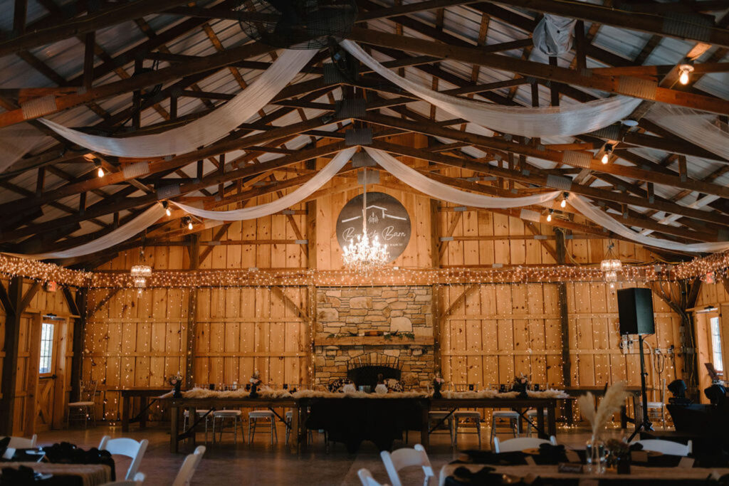 Barn interior set up for a wedding reception with string lights and elegant drapery