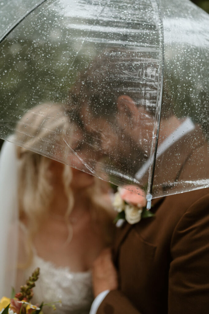 Close-up of a couple under a clear umbrella on their wedding day with raindrops