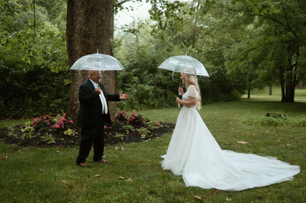 Bride and her father share a moment under umbrellas in a garden