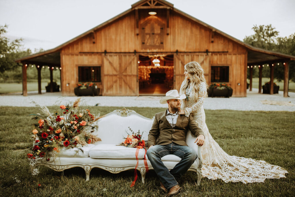 Couple posed on a vintage sofa in front of a barn wedding venue in Indiana