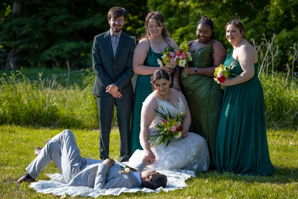 Wedding party with the bride holding her groom laying down the ground