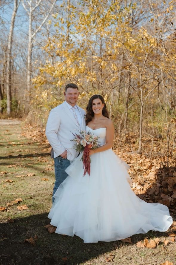 Bride and groom smiling beneath golden trees on their wedding day