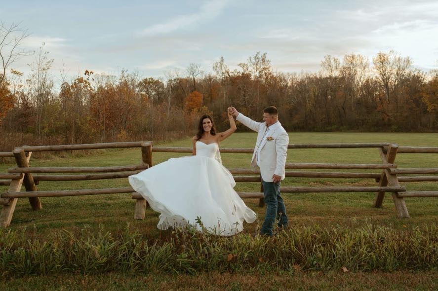 Bride twirling in her gown while groom holds her hand near a wooden fence