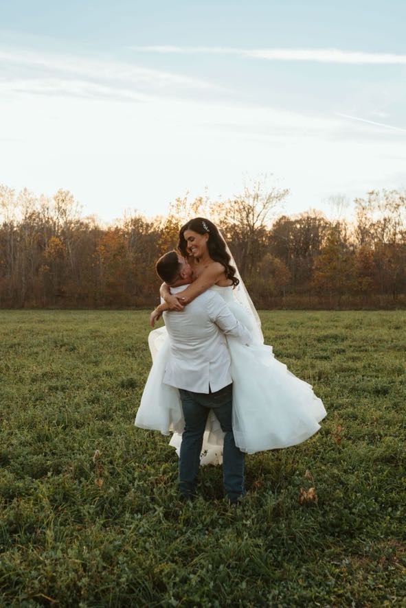 Groom lifting bride joyfully in a grassy meadow during golden hour