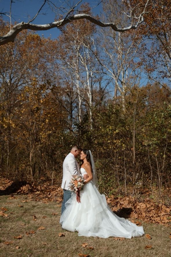 Romantic kiss between bride and groom surrounded by trees during their fall foliage wedding