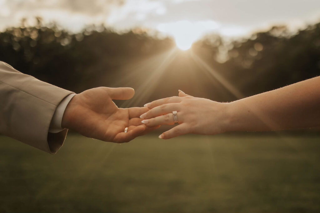 A bride and groom are holding hands with the sun shining through the trees in the background.