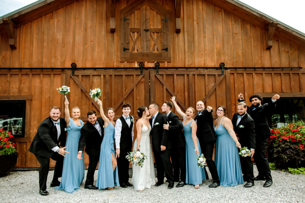 A bride and groom are posing for a picture with their wedding party in front of a barn.