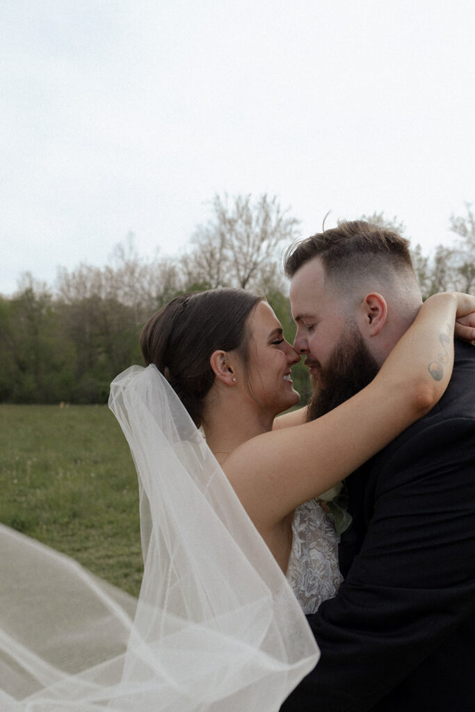 A bride and groom are hugging and kissing in a field.