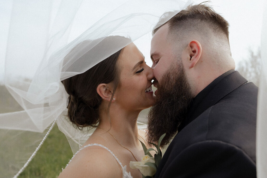 A bride and groom are kissing under a veil.
