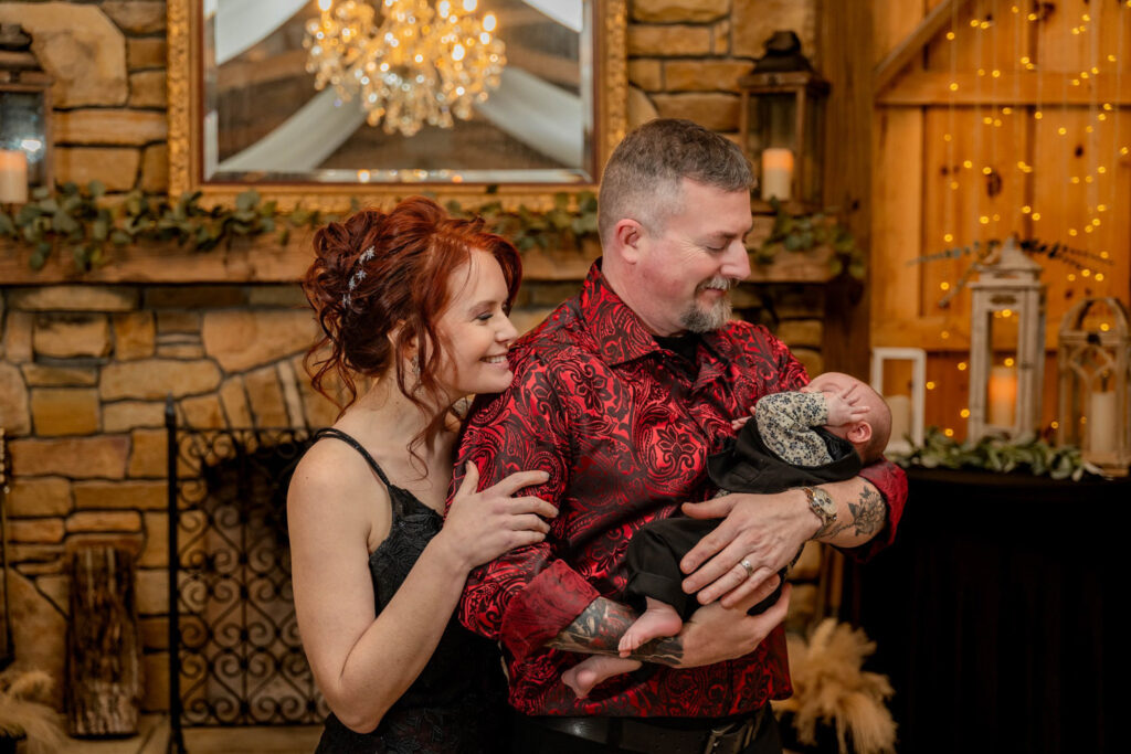 Couple smiling at their newborn baby beside a glowing fireplace