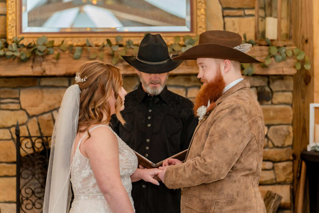 Bride and groom exchanging vows in front of a fireplace at a rustic indoor wedding venue