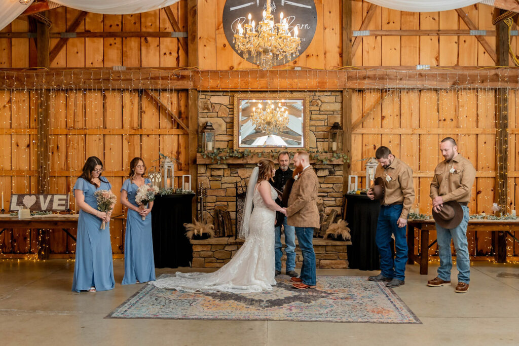 Bride and groom at the altar inside a cozy barn wedding venue with a decorated fireplace