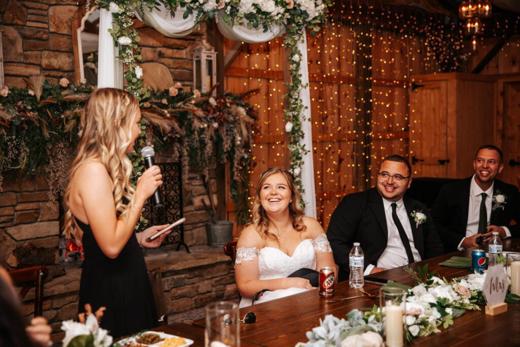 Bride laughing during reception speech in a wedding venue with a decorated fireplace