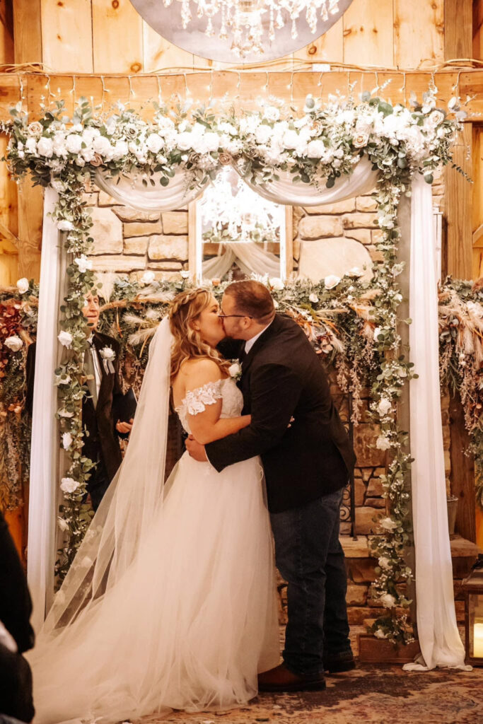 Bride and groom's first kiss in front of a romantic fireplace altar setup