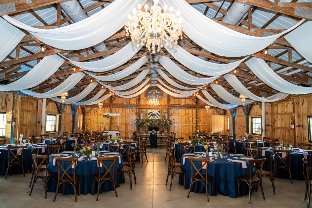 Rustic reception setup with elegant drapery, chandeliers, and a stone fireplace as the focal point of the venue