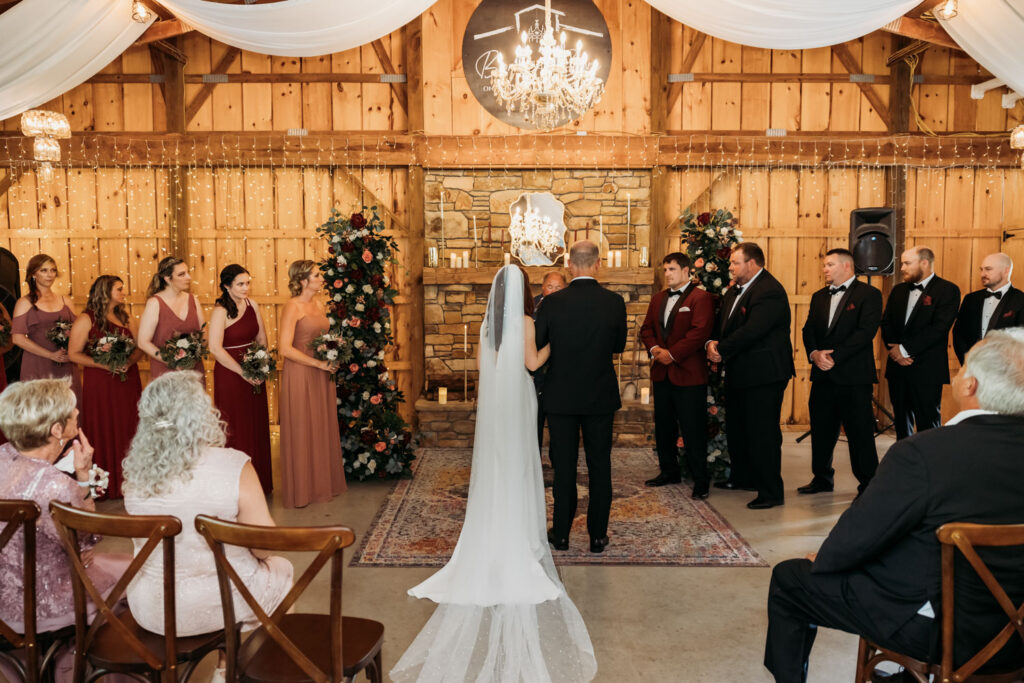 Bride and groom at indoor barn wedding ceremony with bridal party