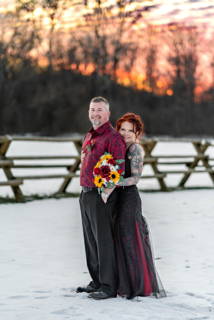 ride and groom embracing in a snowy field at sunset a scenic backdrop often factored into venue pricing for weddings.