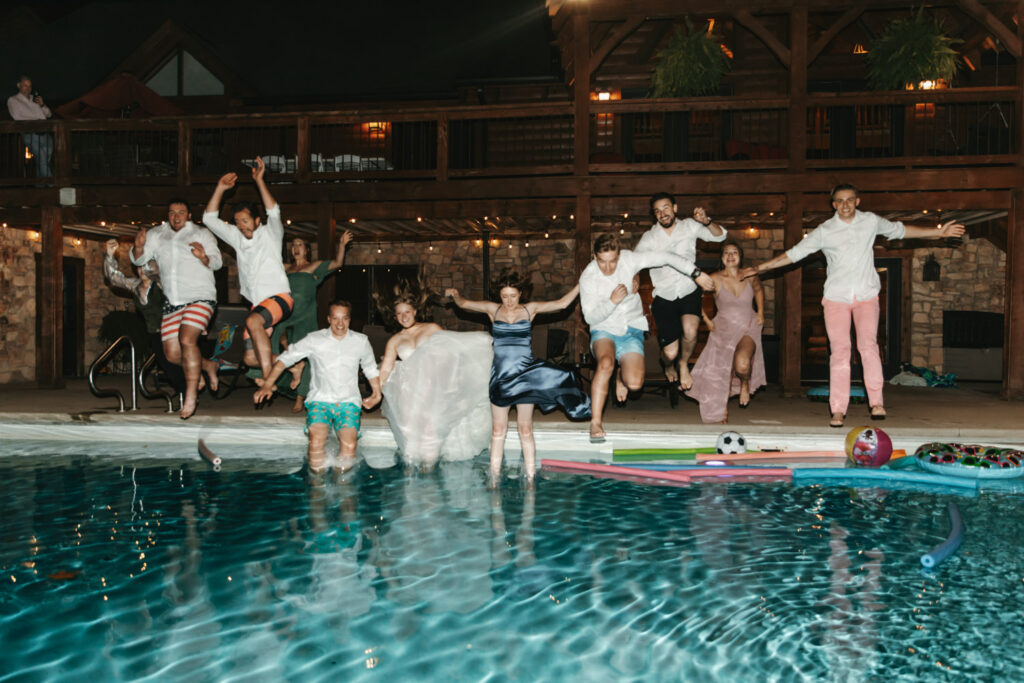 Wedding group jumping into a pool during nighttime celebration