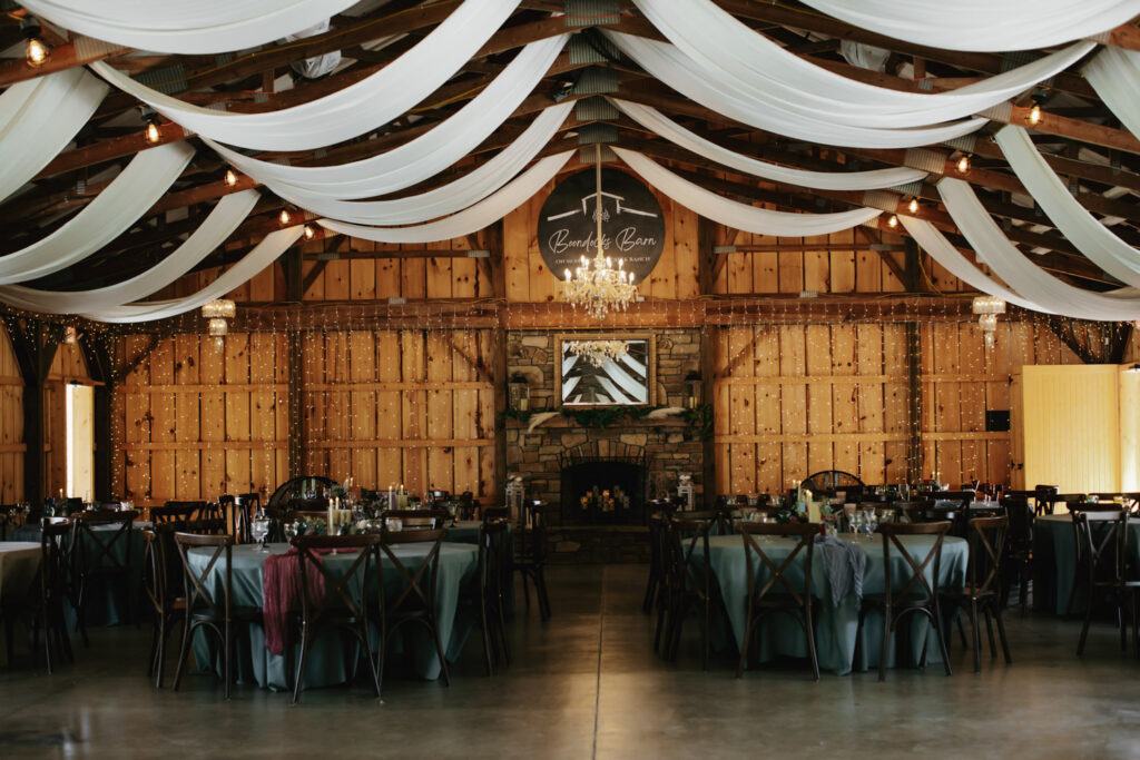 Barn wedding venue decorated with draped fabric and chandeliers illustrating the ambiance couples review when comparing venue pricing for weddings
