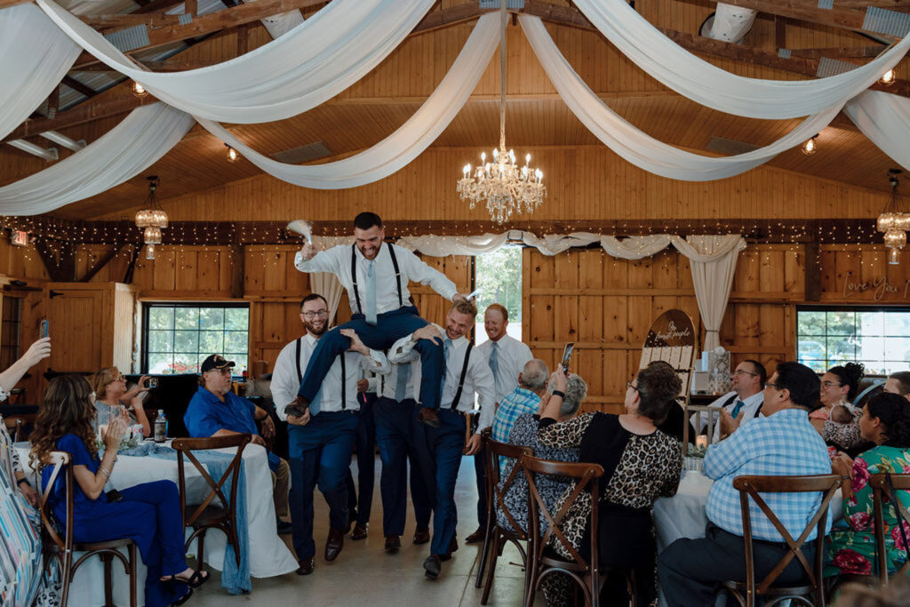 Groomsmen lifting the groom during a lively barn reception
