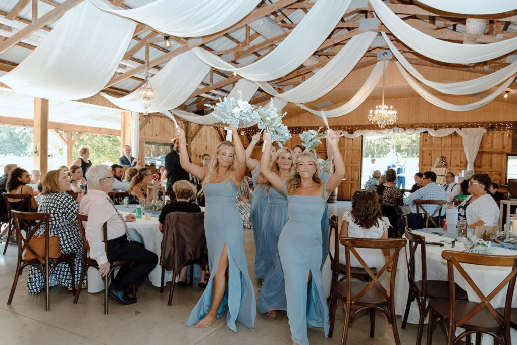 Bridesmaids dancing into a draped barn reception
