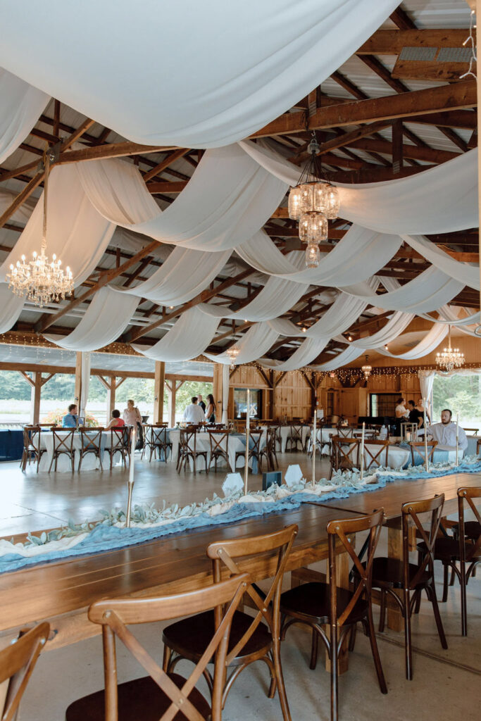 Long tables and soft white draping inside a rustic barn venue