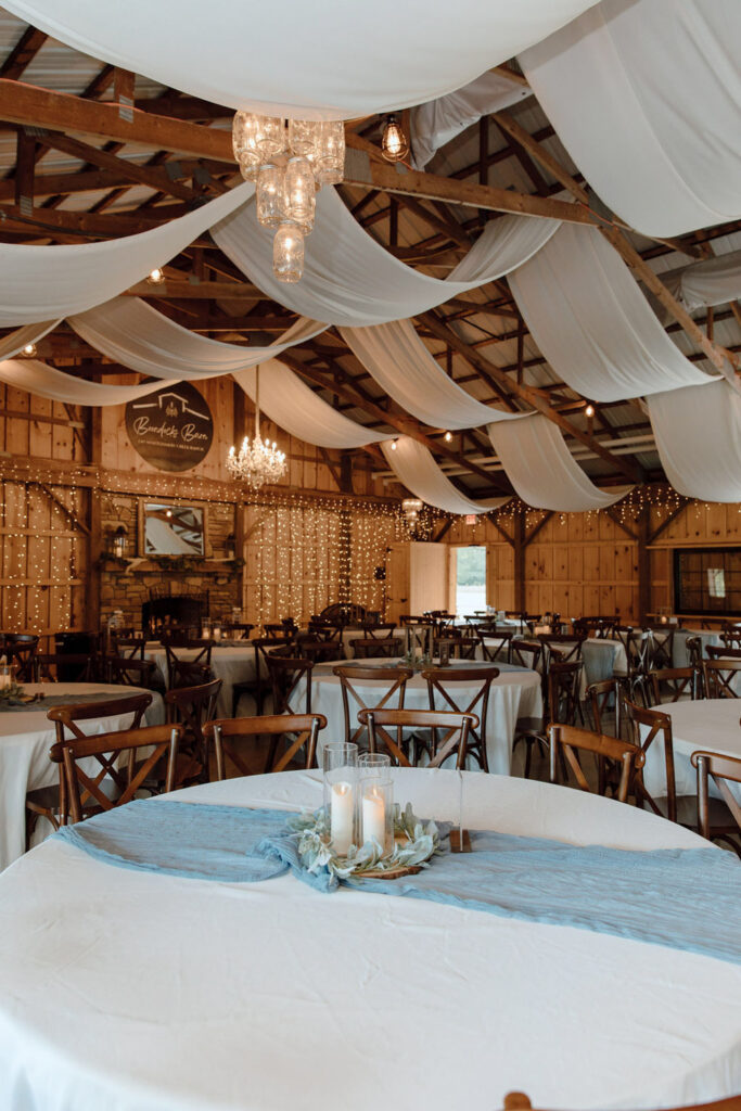 Round guest tables with candle centerpieces inside a wooden barn