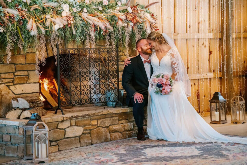 Bride and groom sitting by a stone fireplace indoors, sharing a quiet, intimate moment