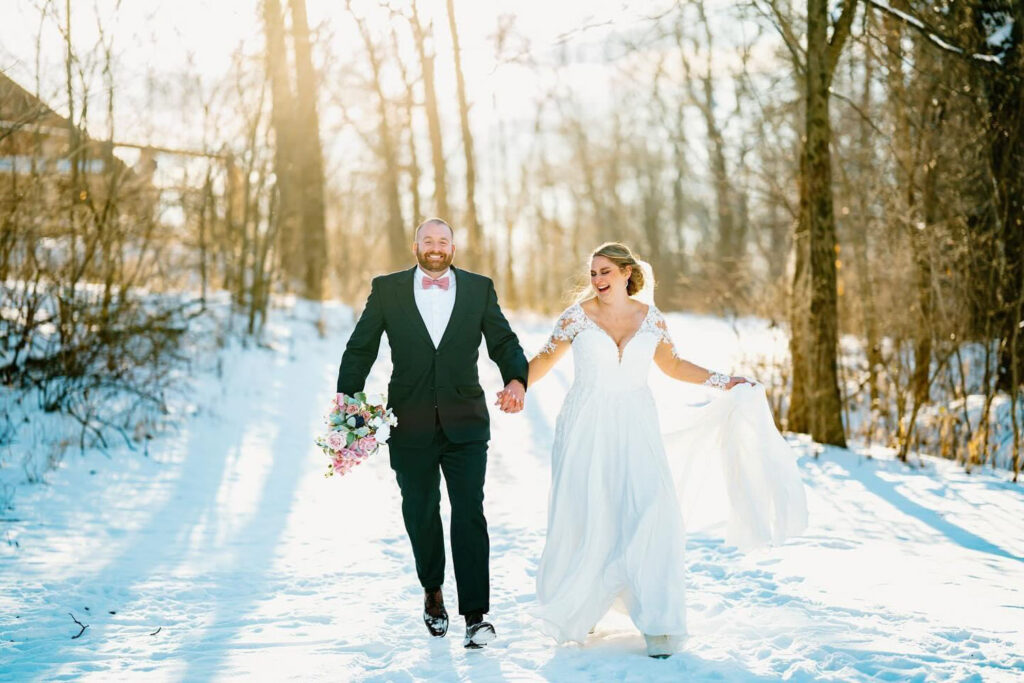 Bride and groom holding hands running through the snow