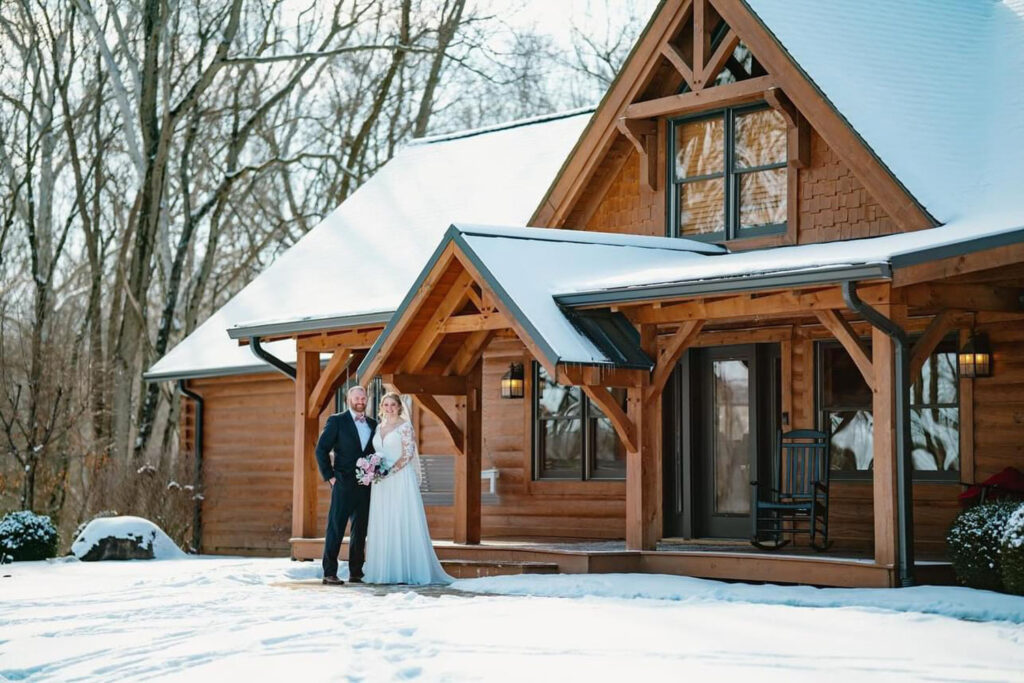 Bride and groom standing together outside a snow-covered rustic wooden lodge.