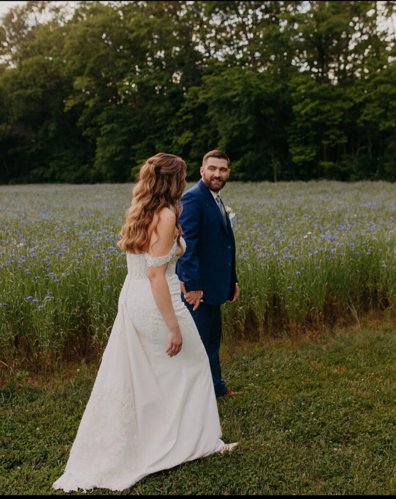 Bride and groom holding hands walking through a wildflower field.