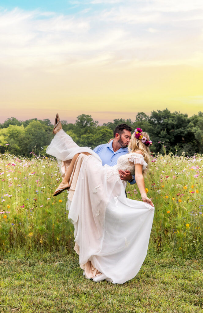 Groom lifting and kissing bride in a wildflower field at sunset.