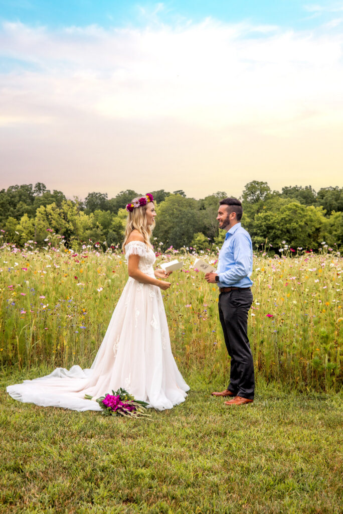 Bride and groom reading vows to each other in a blooming meadow.
