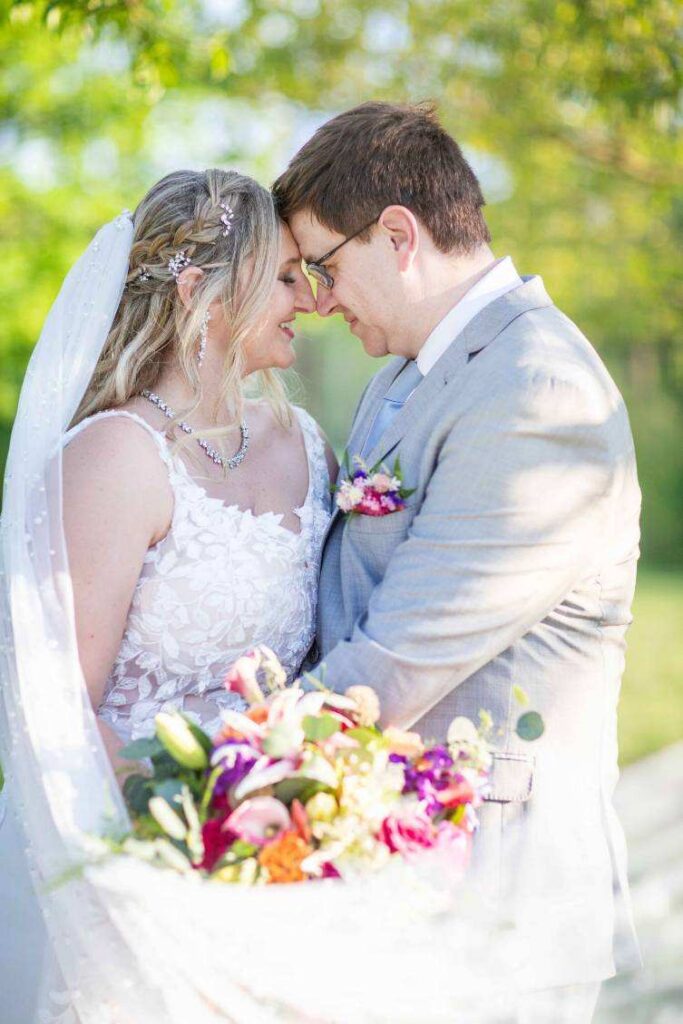 Bride and groom embracing with bright bouquet in soft sunlight