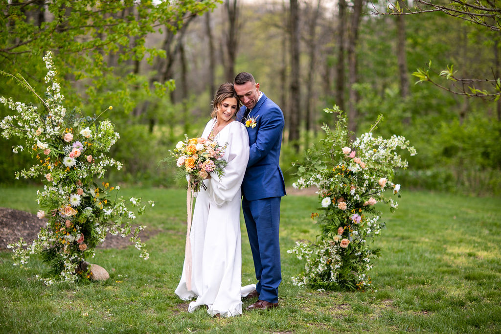 Couple standing between floral ceremony arrangements in a garden
